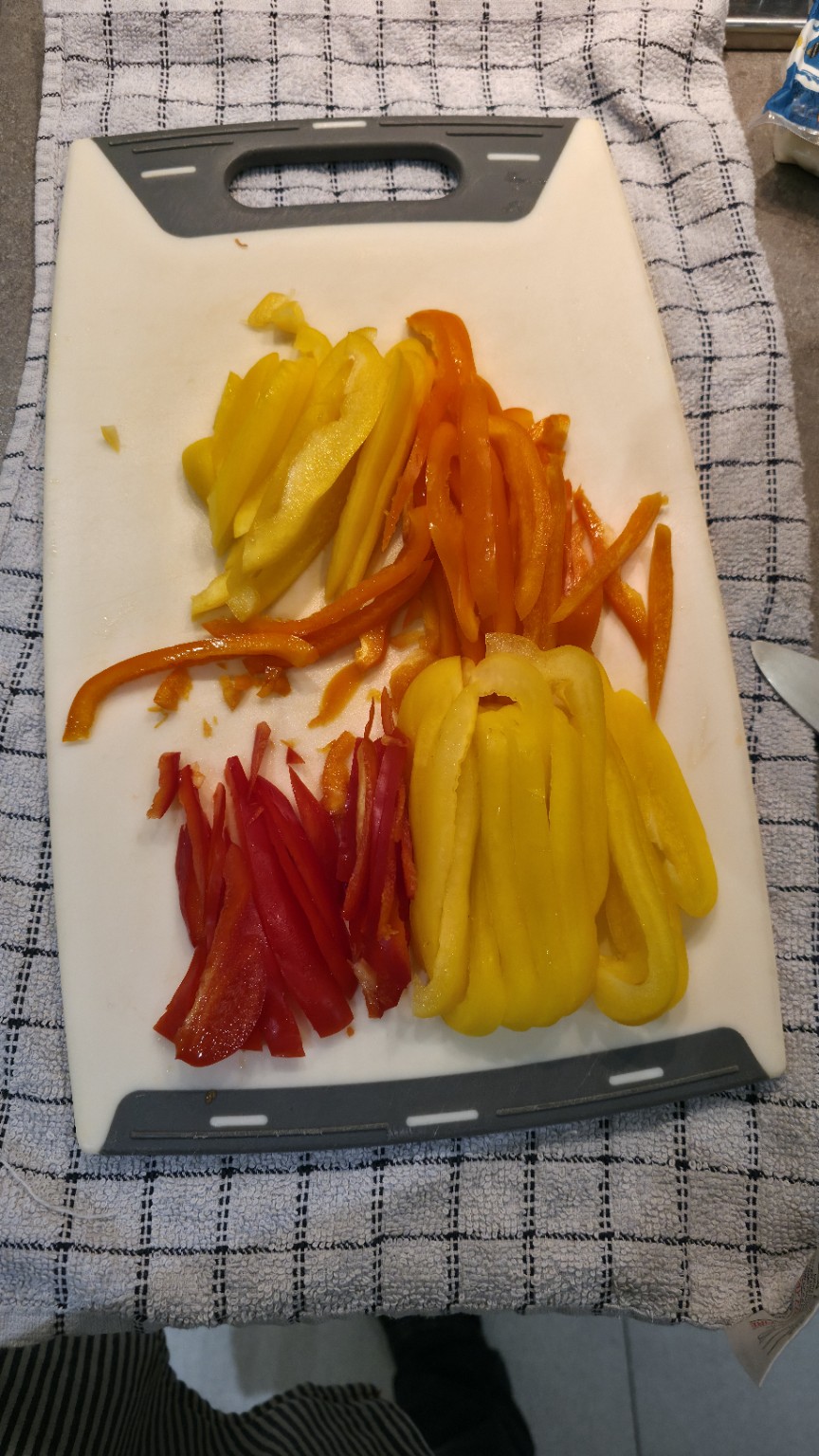 Red orange and yellow peppers sliced into strips on a white chopping board