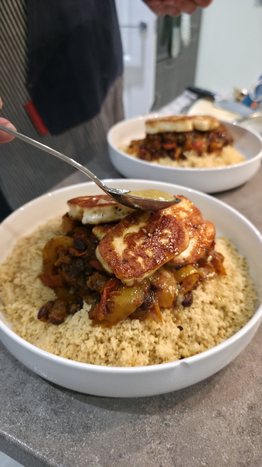 Lemon garlic and honey dressing being spooned over browned halloumi and black bean couscous