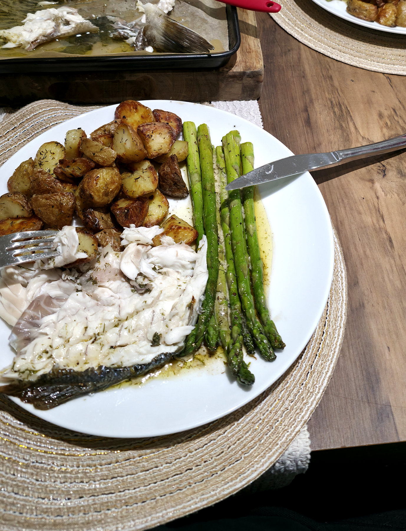 Actual home-cooked sea bass with roasted potatoes and green vegetables served on a white plate