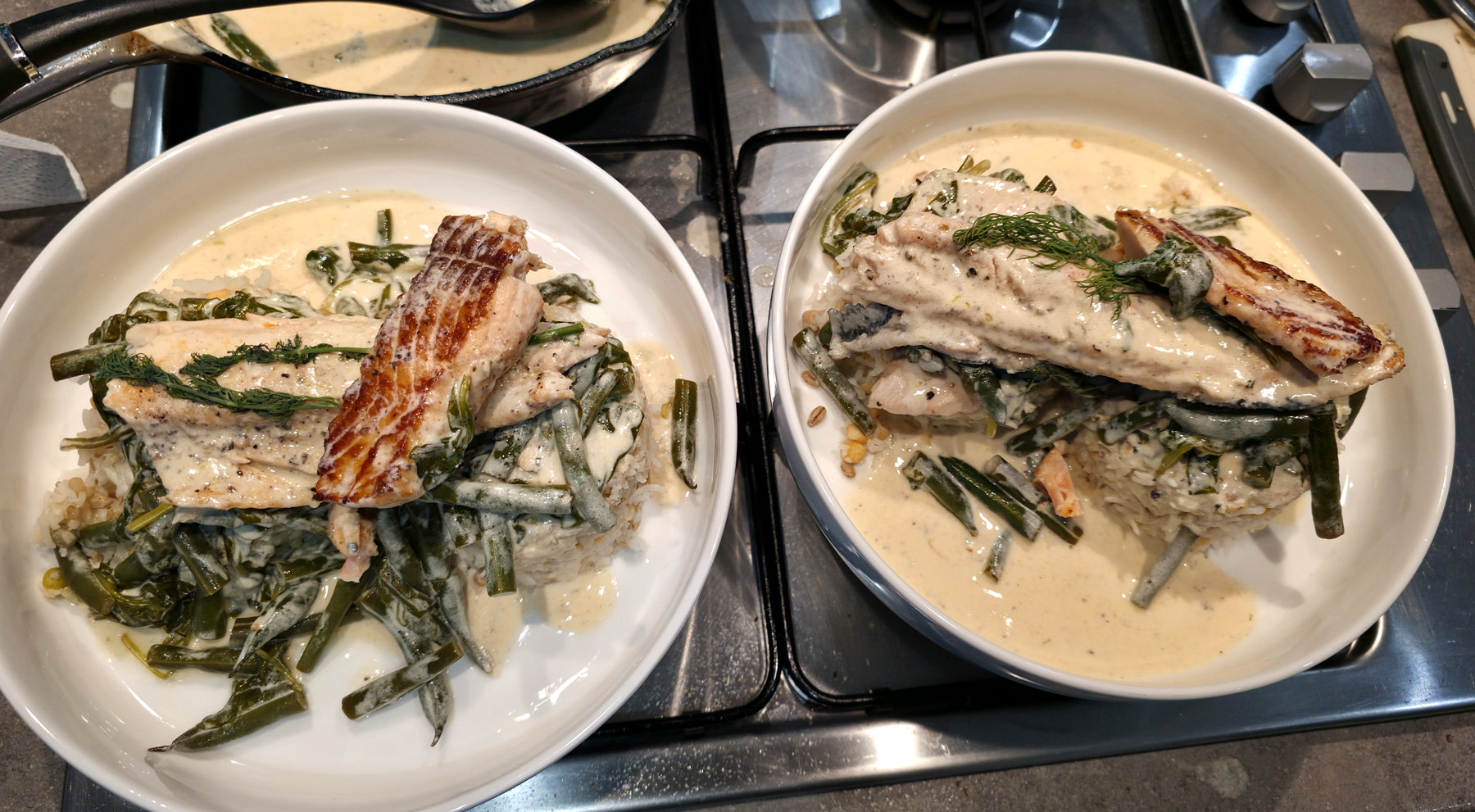 Two salmon portions in creamy sauce with green vegetables in shallow bowls