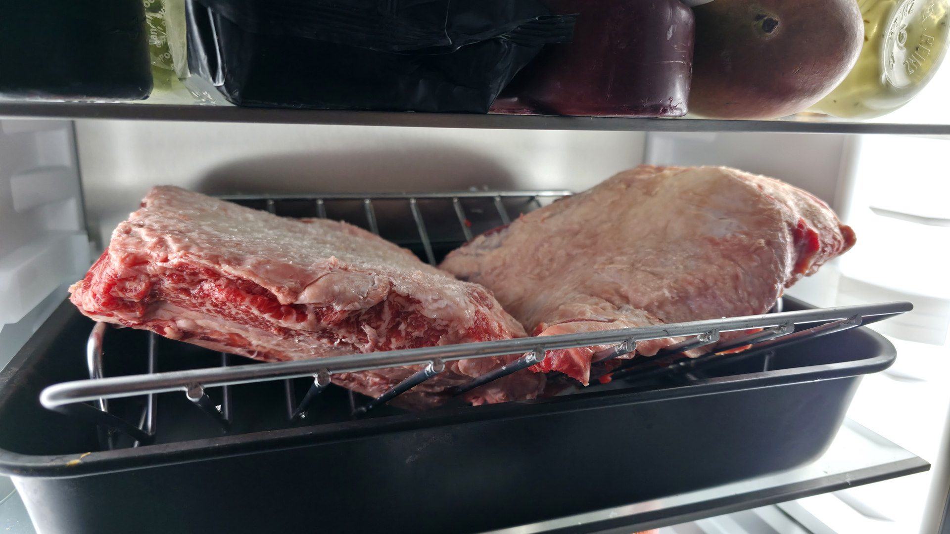 Uncooked beef short ribs resting on a wire rack in a tray inside the fridge during dry-brining