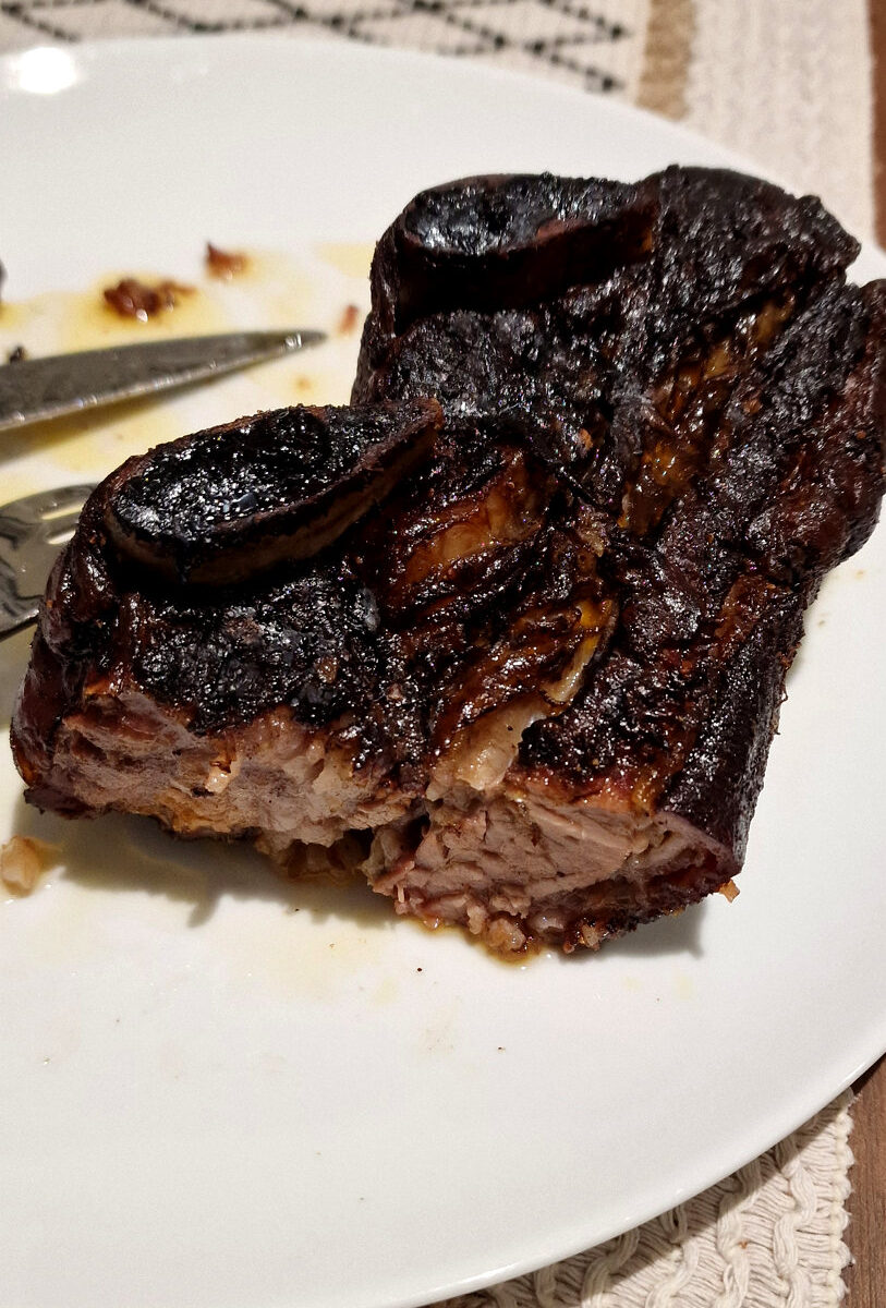 Beef short rib with dark smoked bark and bone on a dinner plate