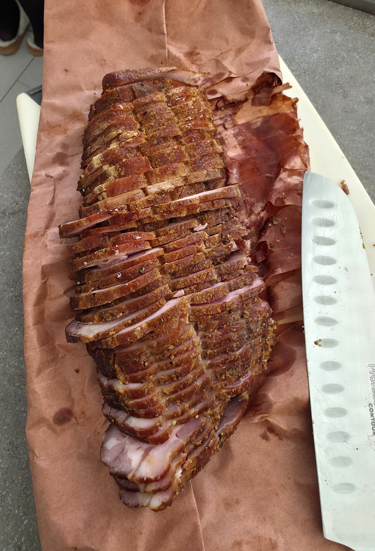 Home-smoked pork sliced on butcher paper beside a kitchen knife
