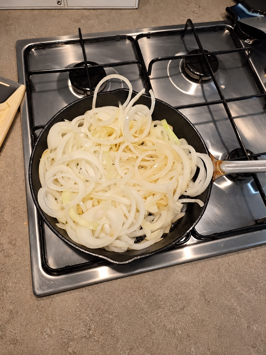 Freshly sliced onions in a black cast-iron skillet on the gas hob before caramelising