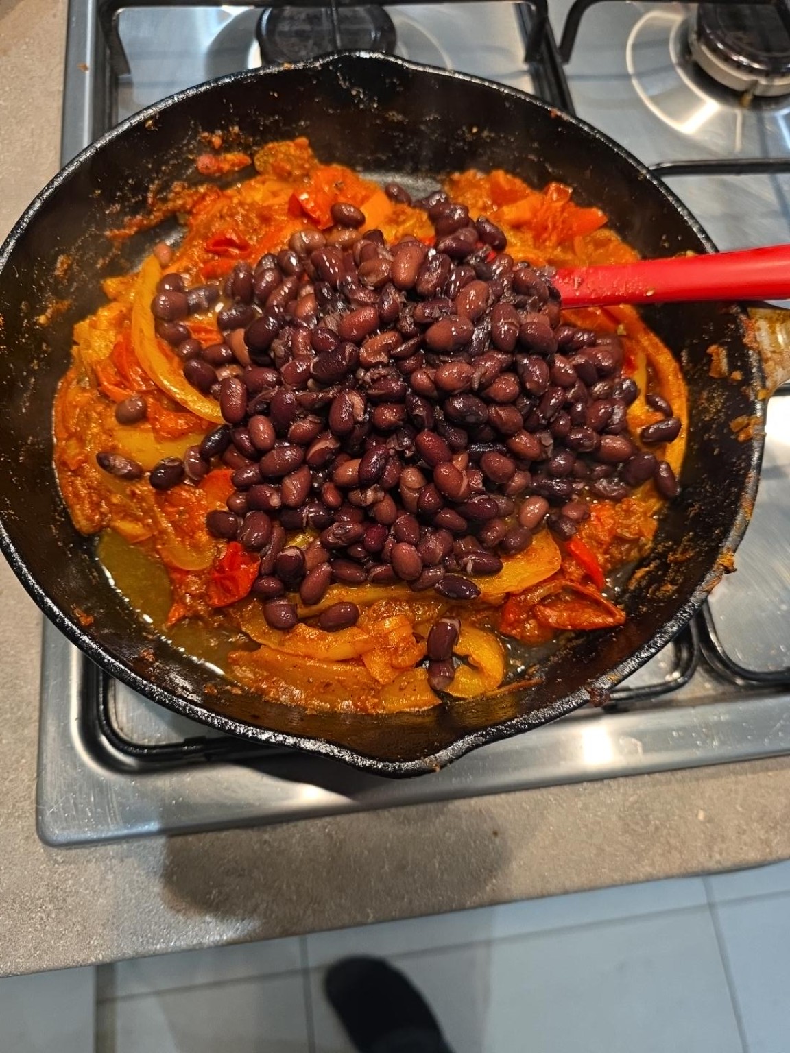 Drained black beans added to the centre of a cast-iron pan with peppers and smoky tomato sauce