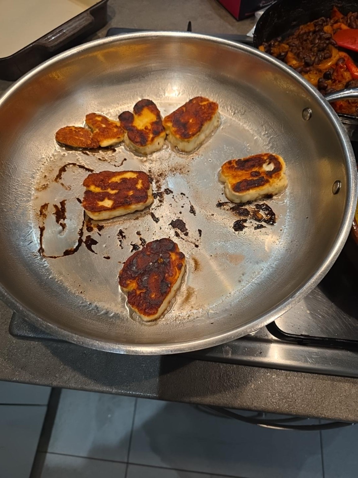 Thick slices of halloumi with deep golden crusts in a stainless steel frying pan