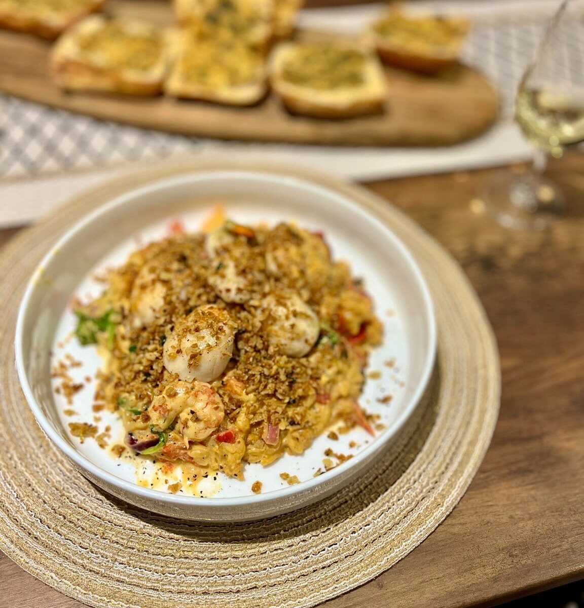 A white bowl of creamy feta and tomato orzo topped with seared scallops and golden lemon panko breadcrumbs