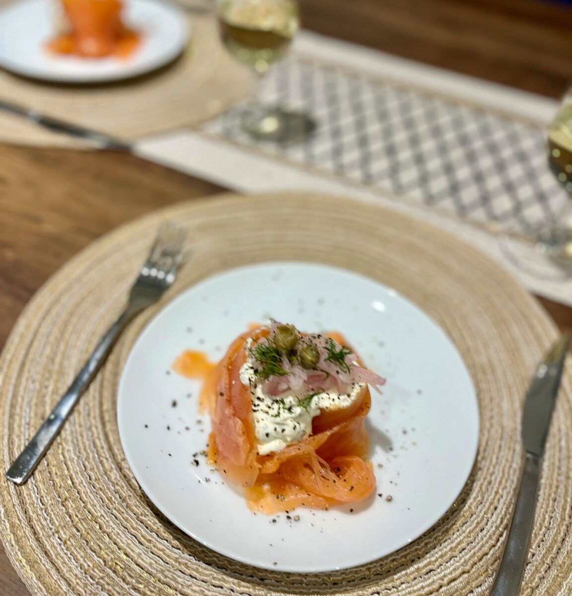 Smoked salmon folded around a creamy dill filling with pink pickled shallots and capers on a white starter plate