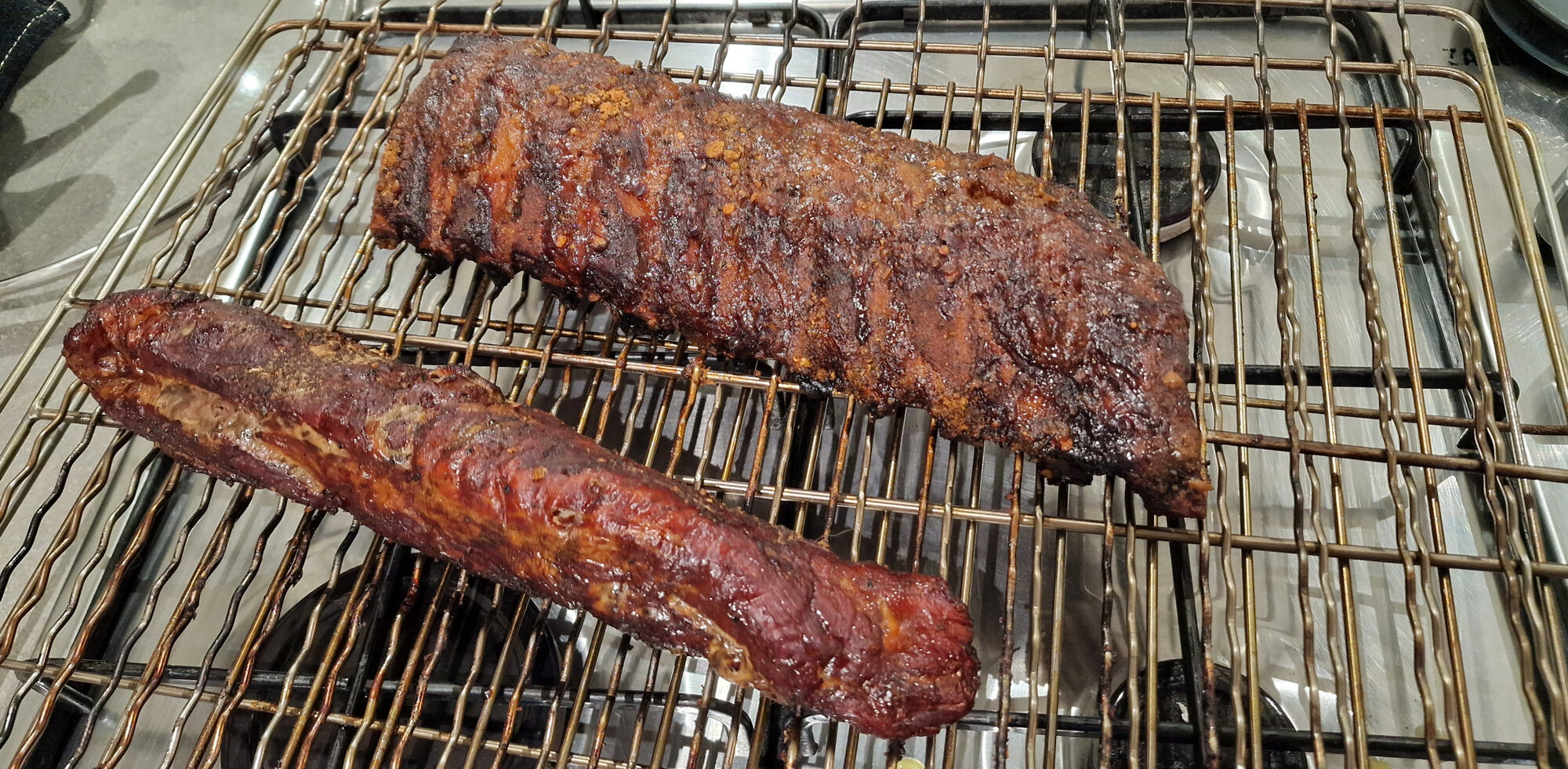 Two pieces of dark amber smoked pork resting on a metal wire rack on the kitchen hob