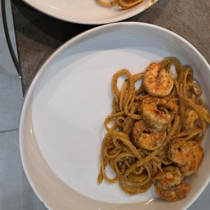 Finished white-wine prawn linguine in a white bowl with golden prawns and glossy sauce