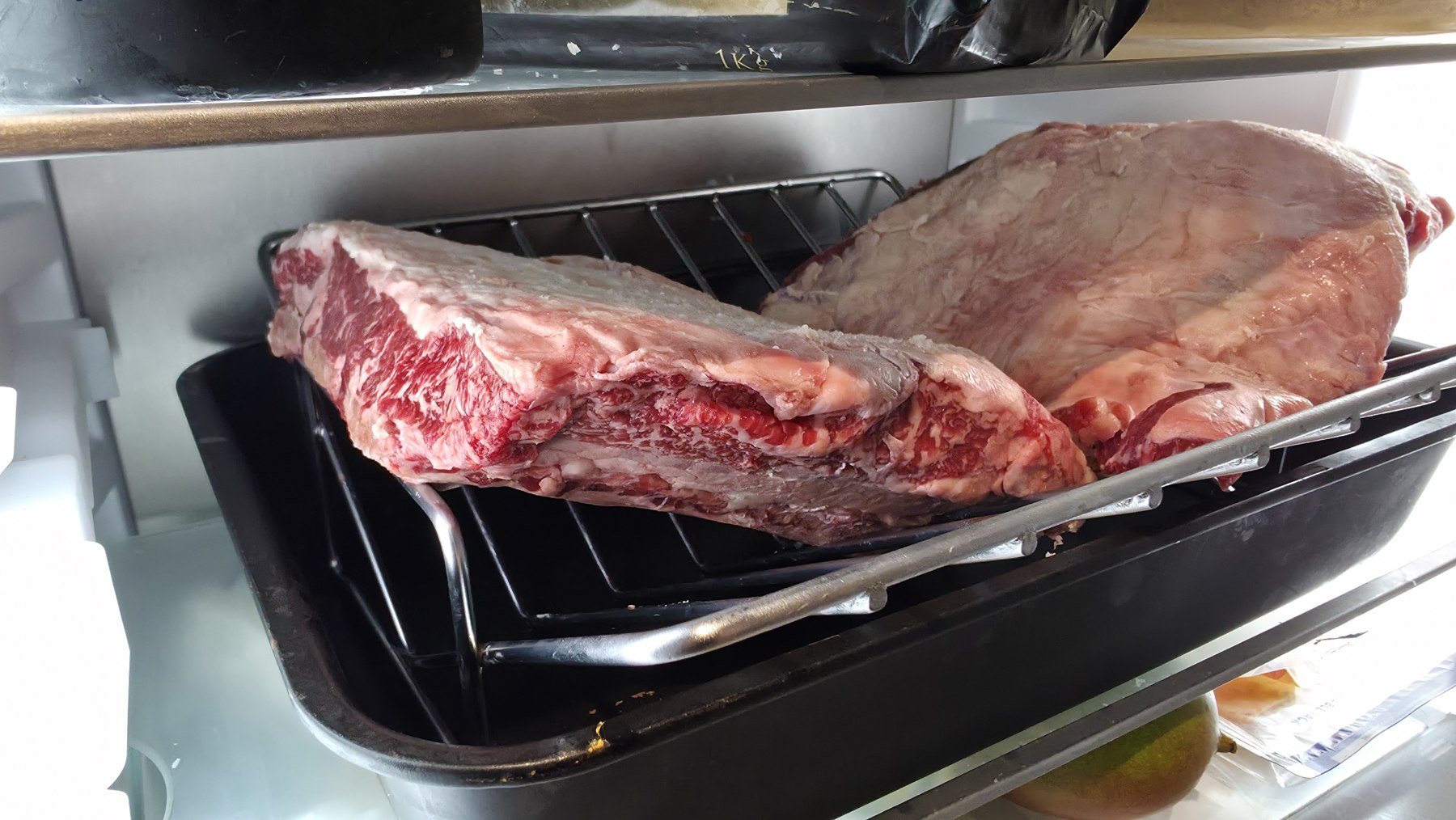 Uncooked beef short ribs resting uncovered on a rack inside the fridge several hours after the first photograph