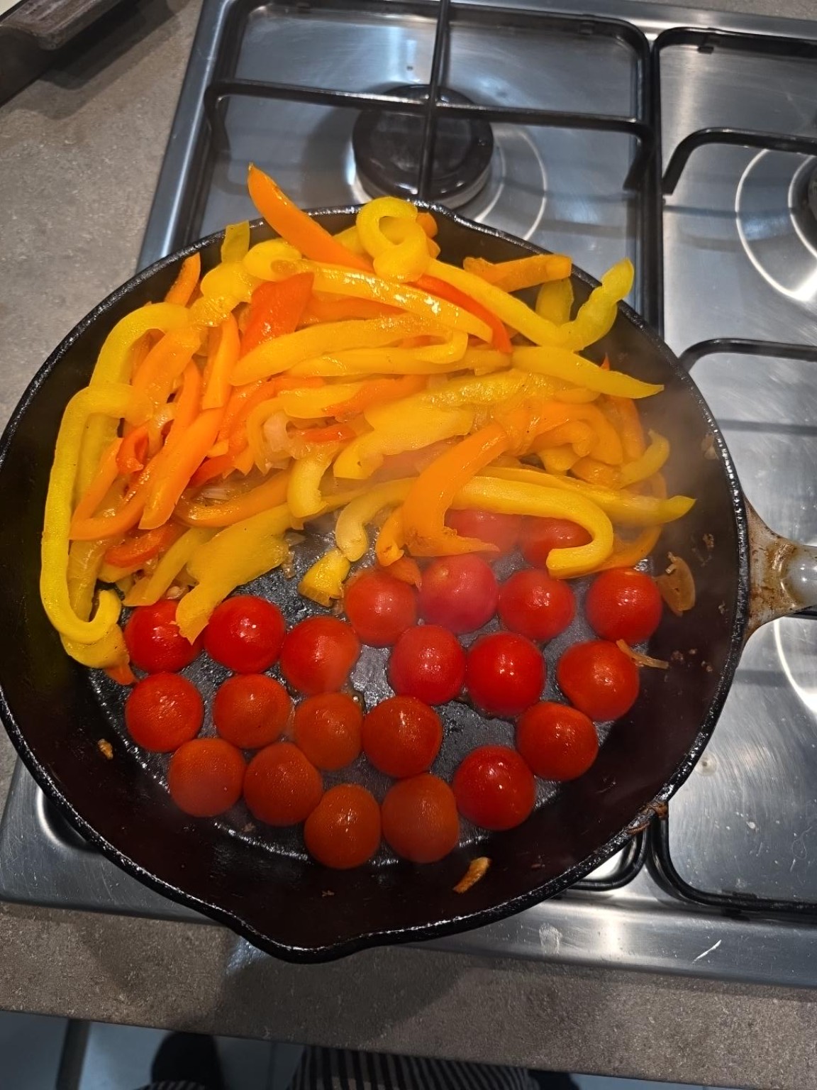 Halved cherry tomatoes placed cut-side down in cast iron with red, orange and yellow peppers